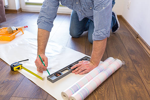 handyman measuring wallpaper to cut on the floor